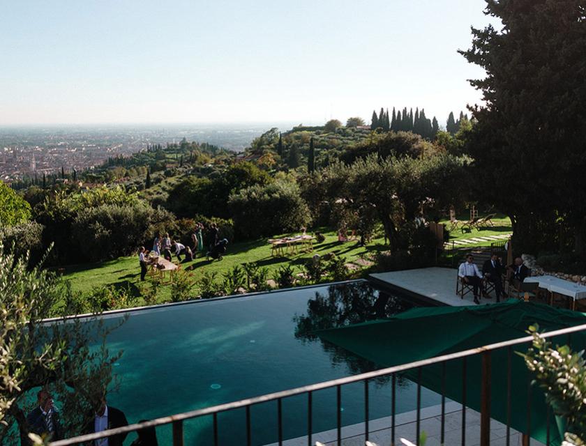 Piscina con vista panoramica sulla città, circondata da alberi e arredi da esterno.