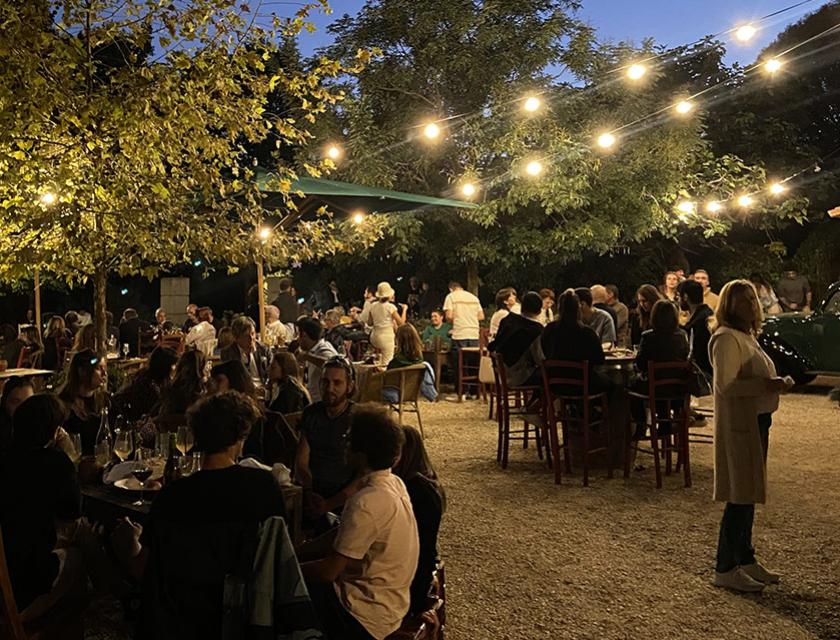 Serata all'aperto con luci sospese e persone che cenano in un'atmosfera conviviale.